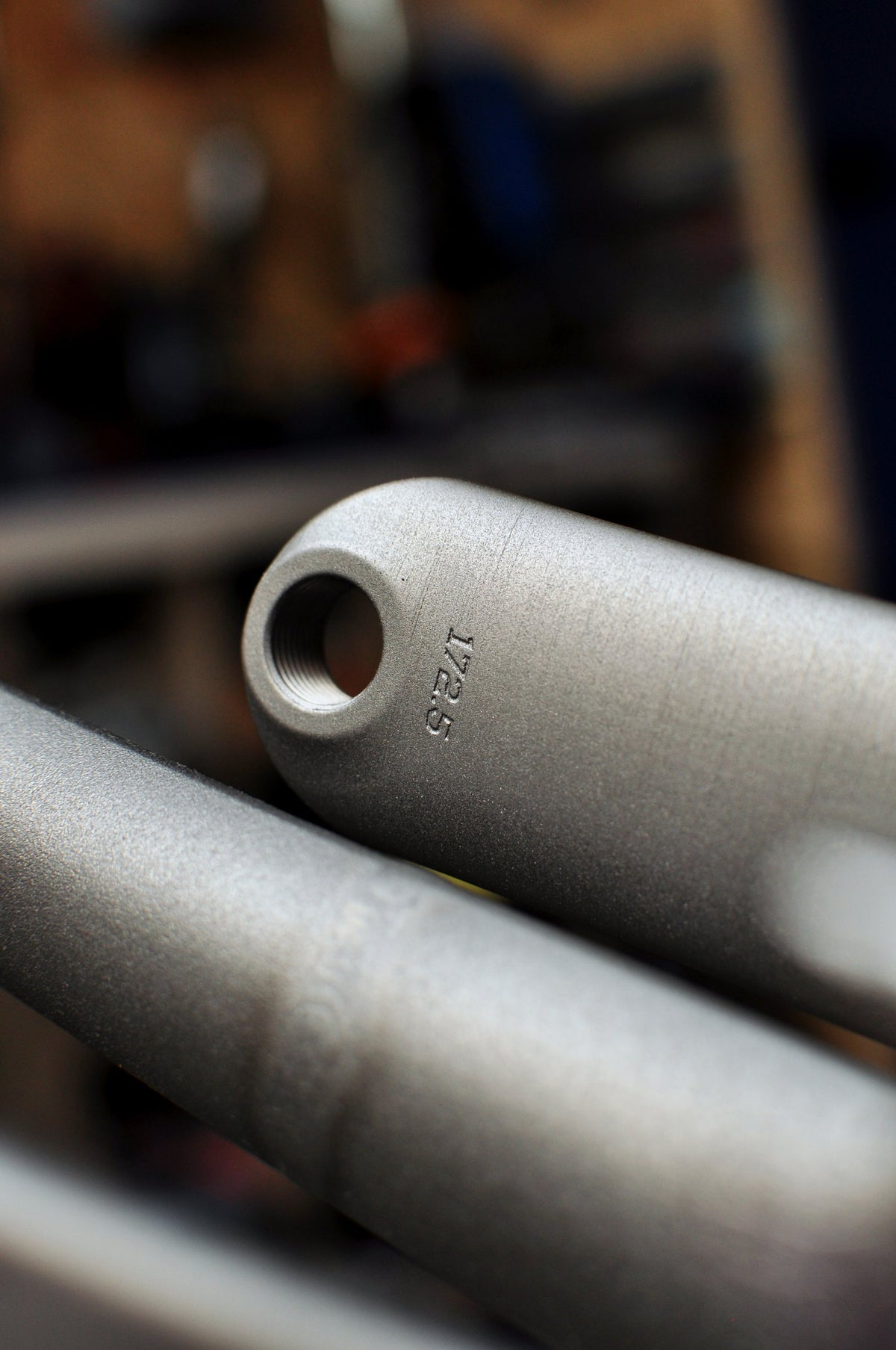 Shot-peened titanium crank arm end engraved with its length, workshop behind, close-up
