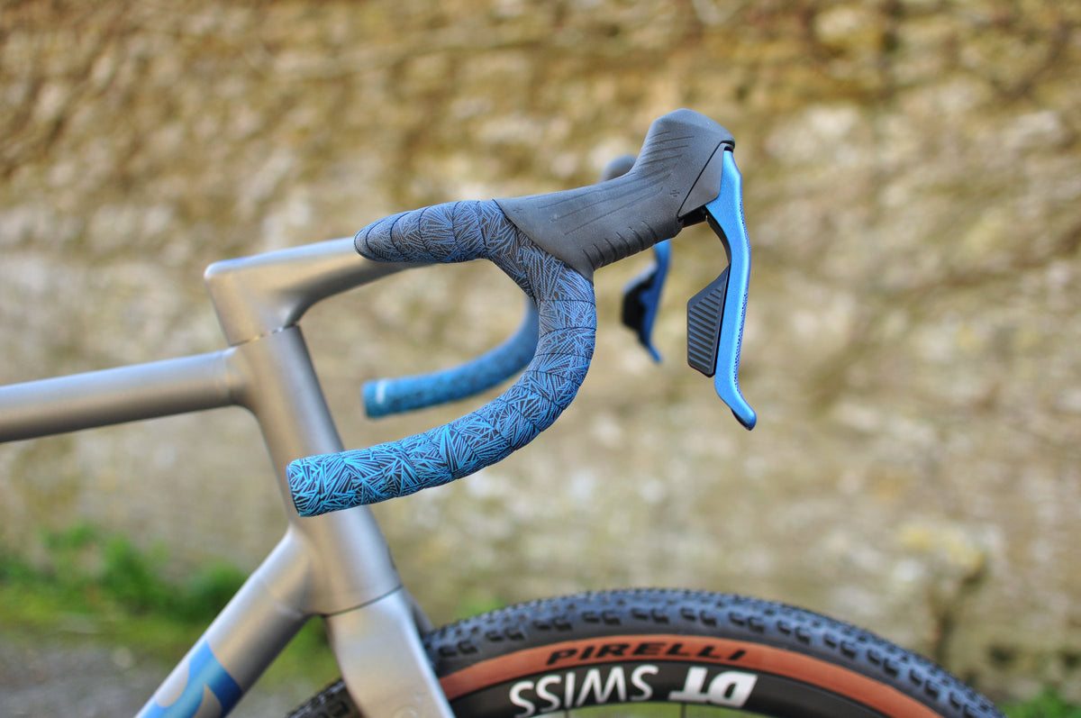 Titanium gravel bike drop bars with patterned blue bar tape and blue brake levers