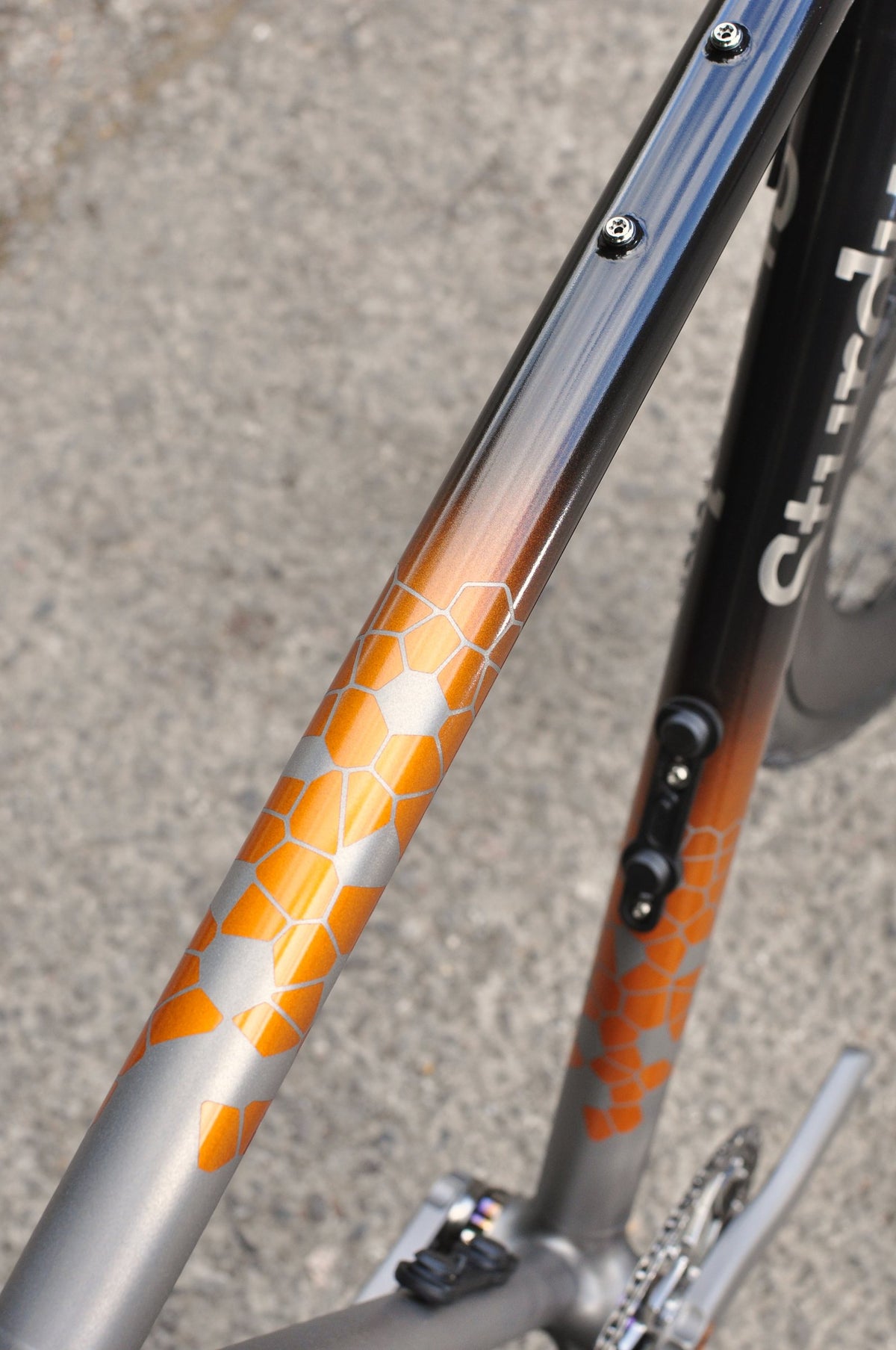 Titanium down tube with orange hexagon pattern fading up into gloss black paint, close-up