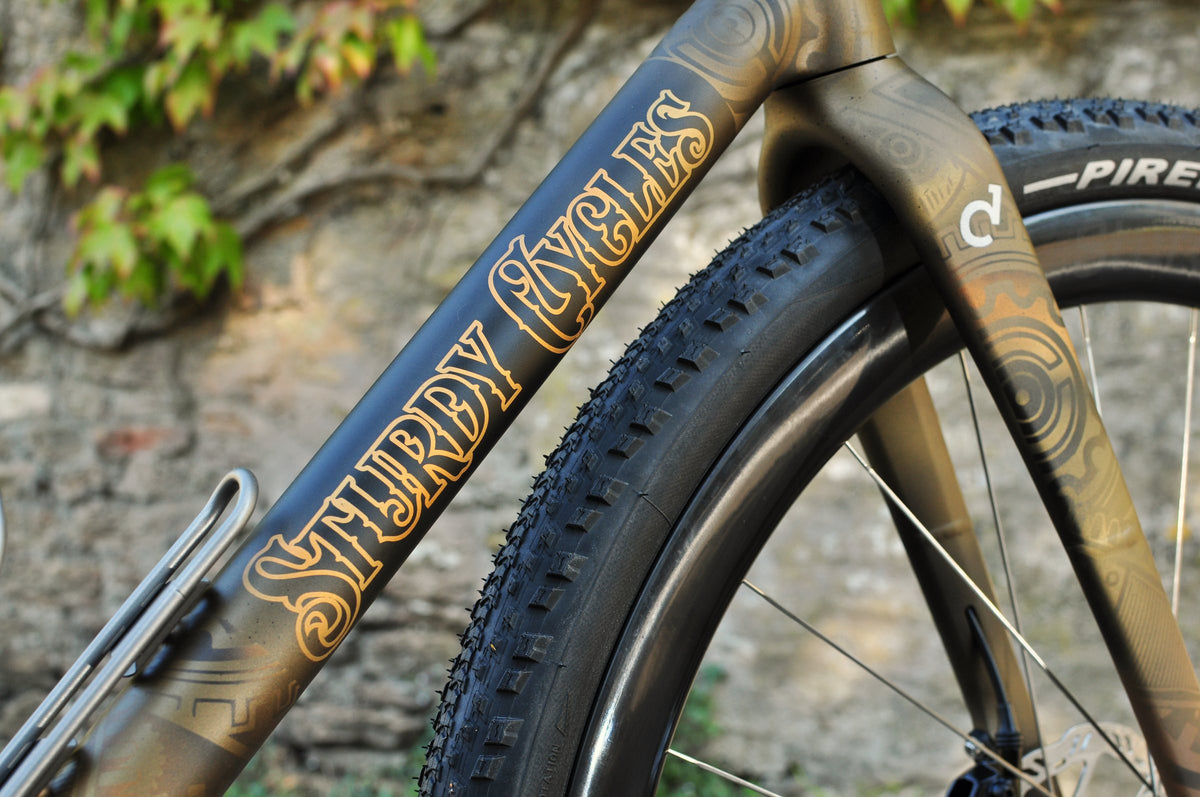 Ornate gold Sturdy Cycles lettering on a bronze down tube with swirling pattern on the fork