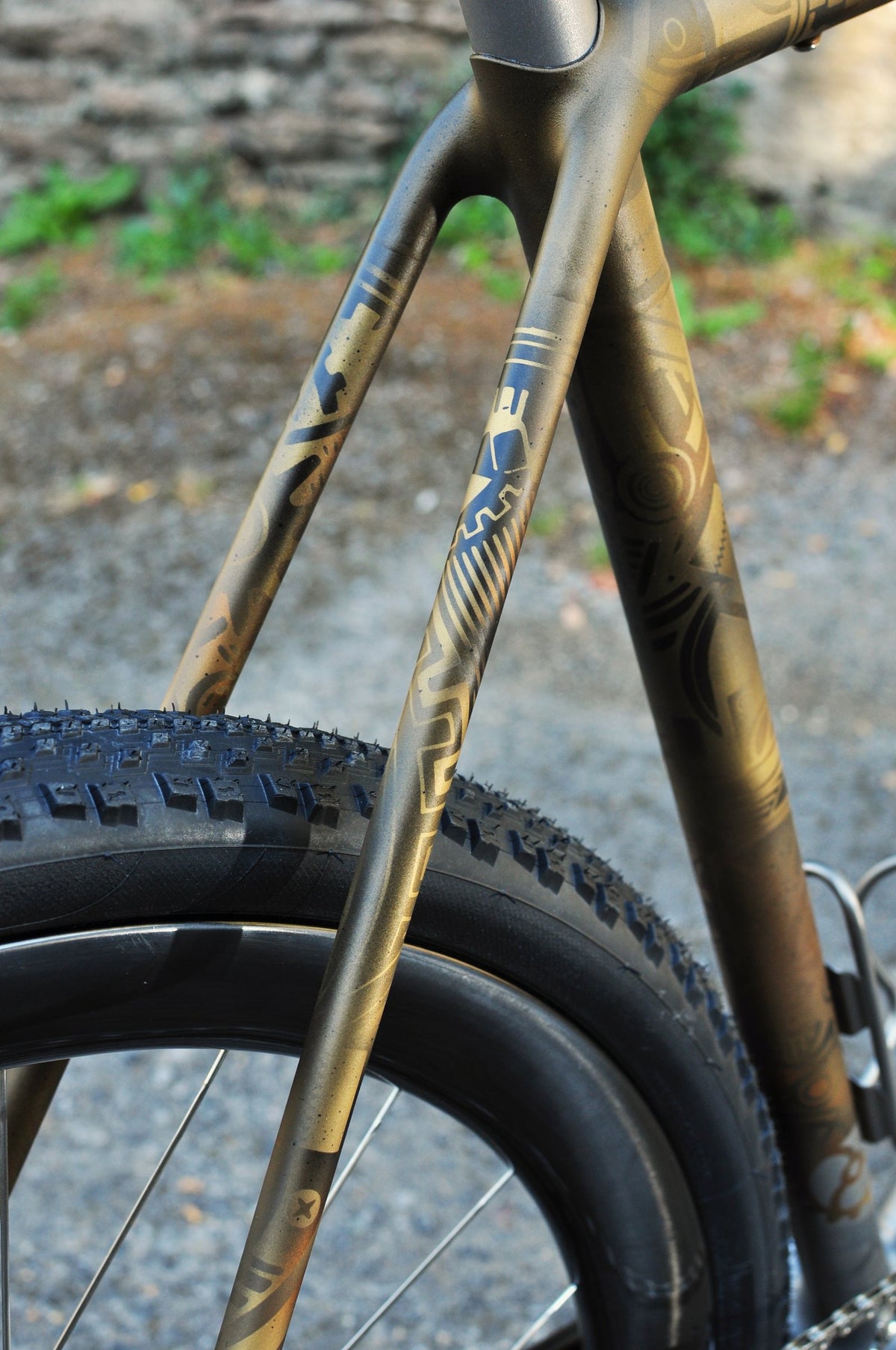 Seat stays and seat tube in bronze tribal-pattern paint above a knobbly gravel tyre