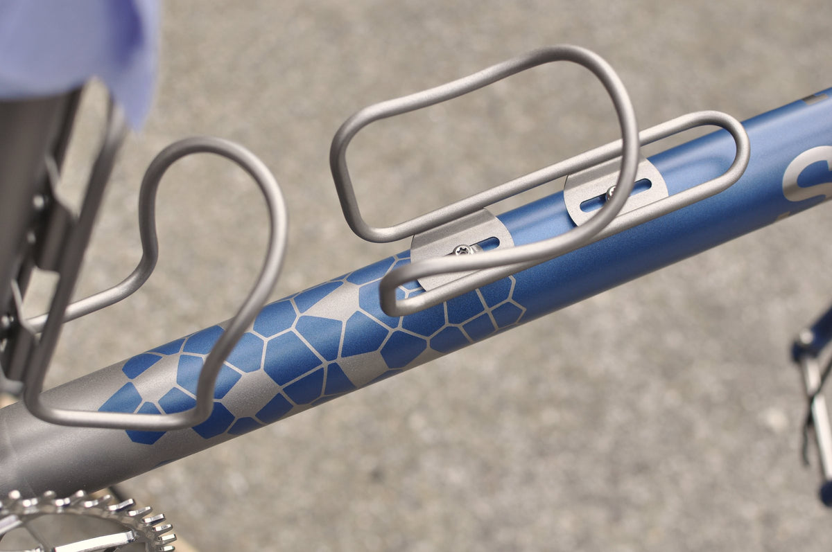 Titanium bottle cages on a down tube with a blue hexagon pattern fading from bare titanium